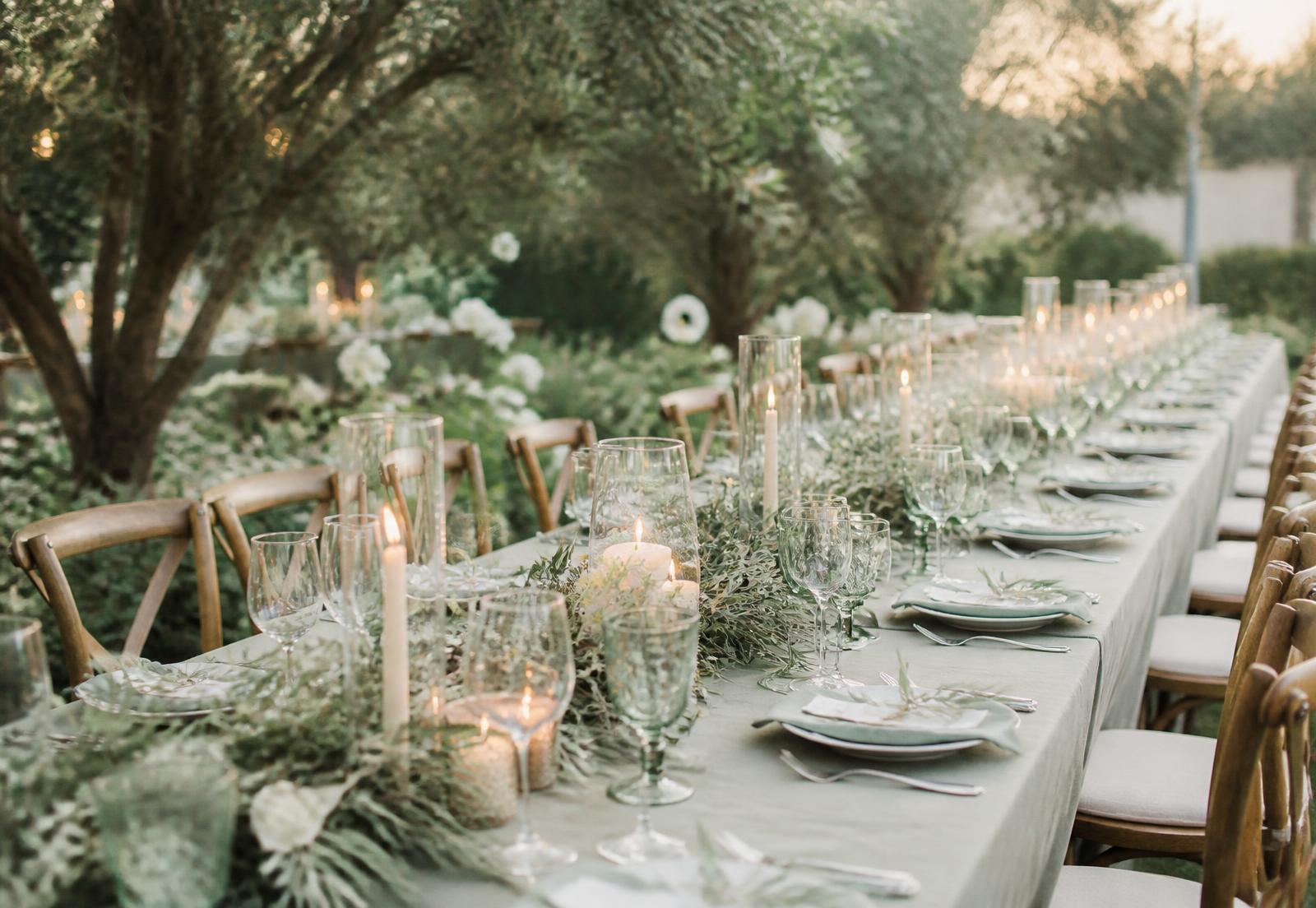 Longue table de mariage décorée de feuillage d'olivier et de bougies au crépuscule